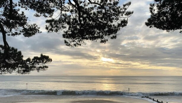 Blick auf einen Strand mit Wellen, Sonnenuntergang und Strandhütten.