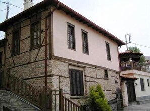 Un edificio de dos pisos con paredes de piedra, un balcón y una escalera que conduce a la entrada.
