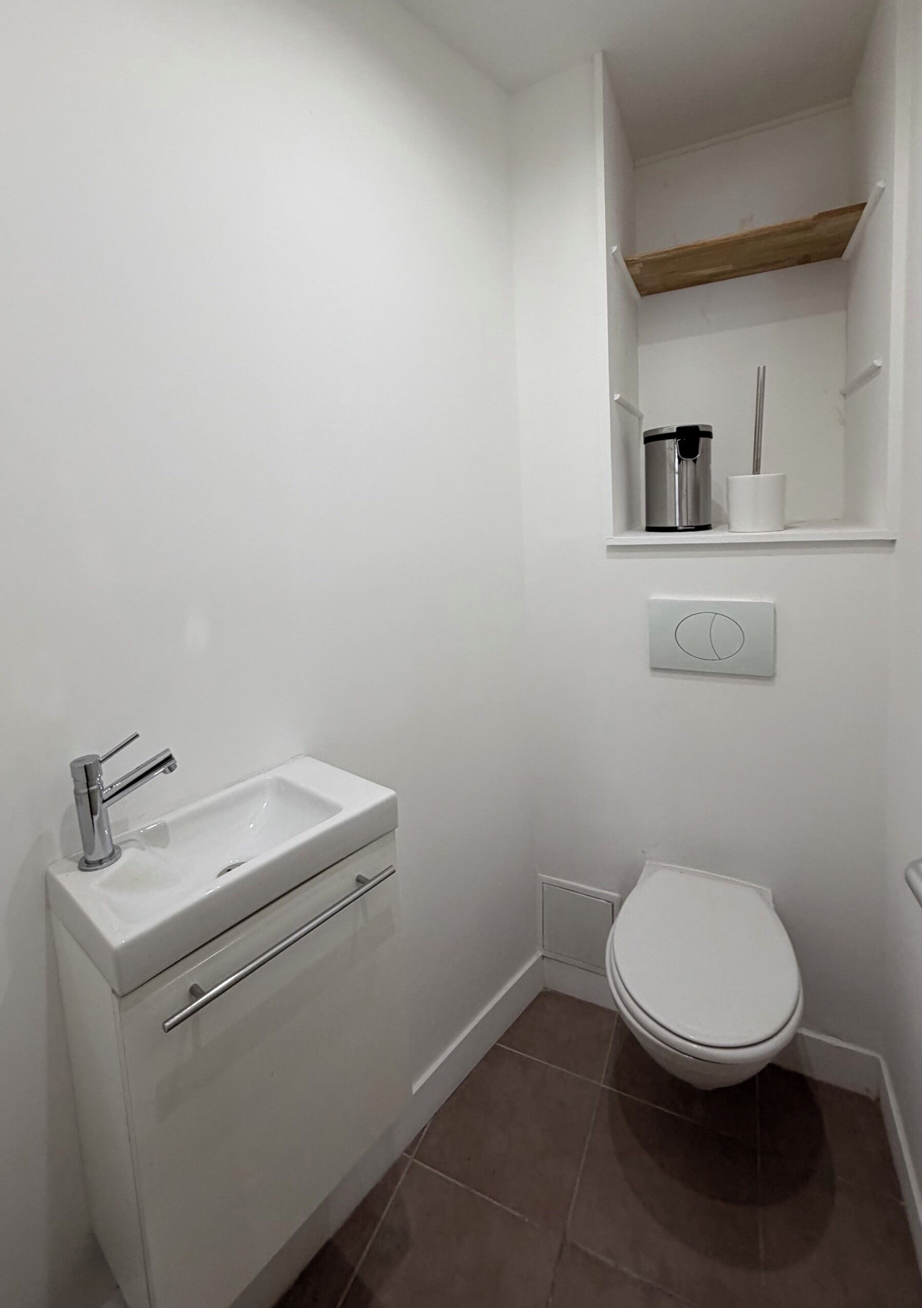 Ein kleines, weißes Badezimmer mit Waschbecken, Toilette und Ablage über der Toilette.