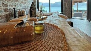 A rustic interior with stone walls, a wooden ceiling, and a large window overlooking a body of water.