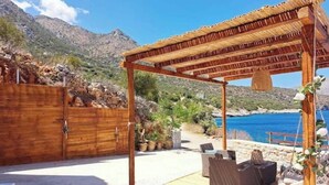 A wooden pergola with a thatched roof, outdoor seating, and a view of the sea.