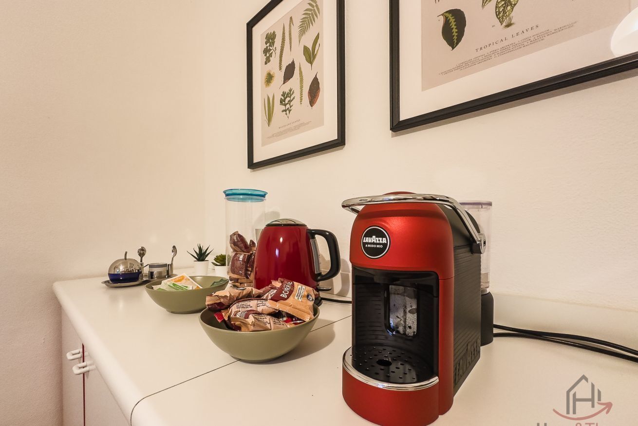 Un plan de travail de cuisine avec une machine à café, un bol de collations, une tasse et une estampe botanique encadrée.