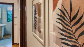 Un passadís amb quadres al mur, una porta que dona a un bany, i vista d'una habitació amb llit.