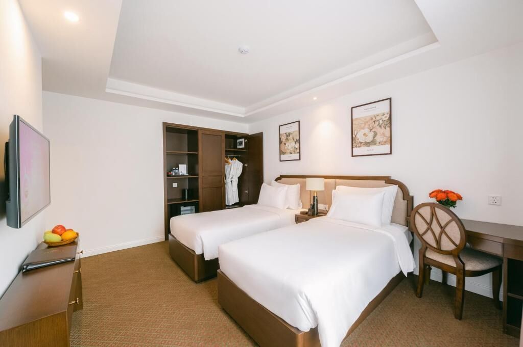 A hotel room with two beds, a desk, a chair, a wardrobe, and a TV.