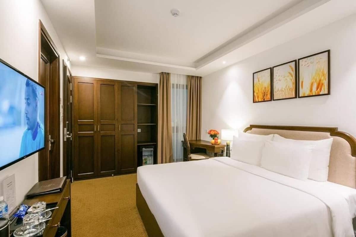 A hotel room with a bed, a desk, a TV, a wardrobe, and artwork on the wall.