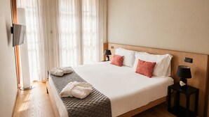 Hotellihuone, jossa on suuri sänky, kaksi yöpöytää, televisio ja ikkuna, jossa on verhot.
