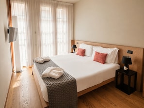 A hotel room with a large bed, two bedside tables, a TV, and a window with curtains.