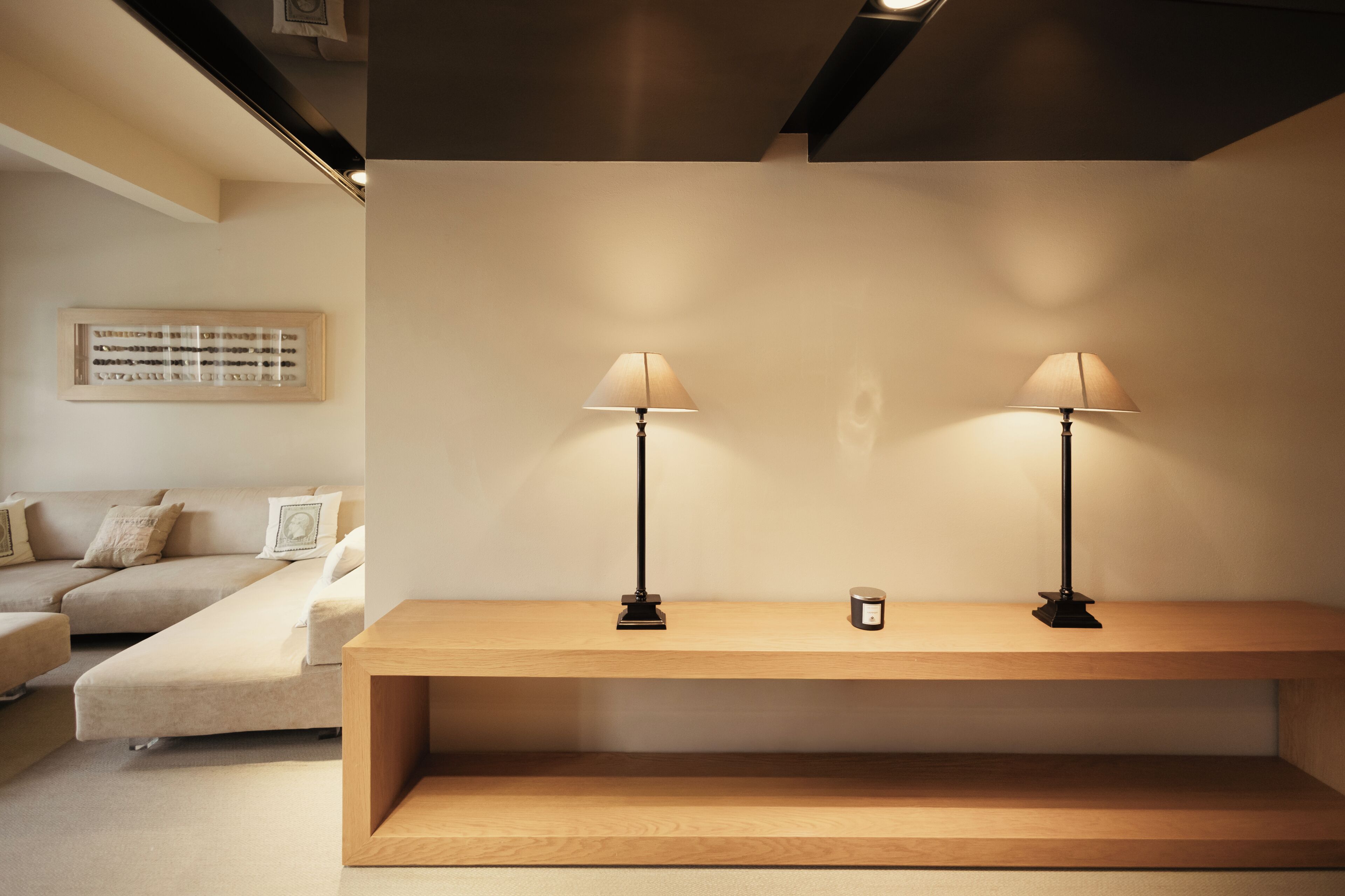 Una sala de estar minimalista con un sofá, dos lámparas sobre una consola de madera y un cuadro en la pared.