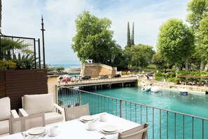 Terraza con una mesa lista para comer, con vista a un cuerpo de agua que incluye barcos y un puente al fondo.