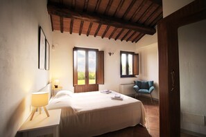 A bedroom with a bed, bedside lamp, two windows, a chair, and a wooden ceiling. - House in the Chianti countryside of the Sienese hills (Toscana)