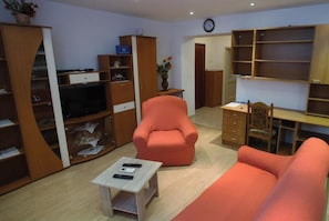 Ein Wohnzimmer mit Sofa, Sessel, Fernseher und Holzregalen.