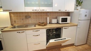 A kitchen with white cabinets, a microwave, a dishwasher, and a refrigerator. - Comfortable Apartment in the Center of Split (Split)