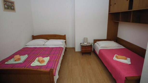 A small, clean room with two beds, wooden headboards, and a nightstand with a lamp. - Comfortable Apartment in the Center of Split (Split)