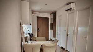 A modern dining area with a table and chairs, a kitchen in the background, and a wooden door. - Jade Leaves Homestay HaLong -Seaview (Hong Gai)
