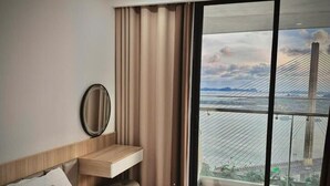 A hotel room with a bed, a bedside table, a mirror, a window with a view of a bridge and cityscape. - Jade Leaves Homestay HaLong -Seaview (Hong Gai)