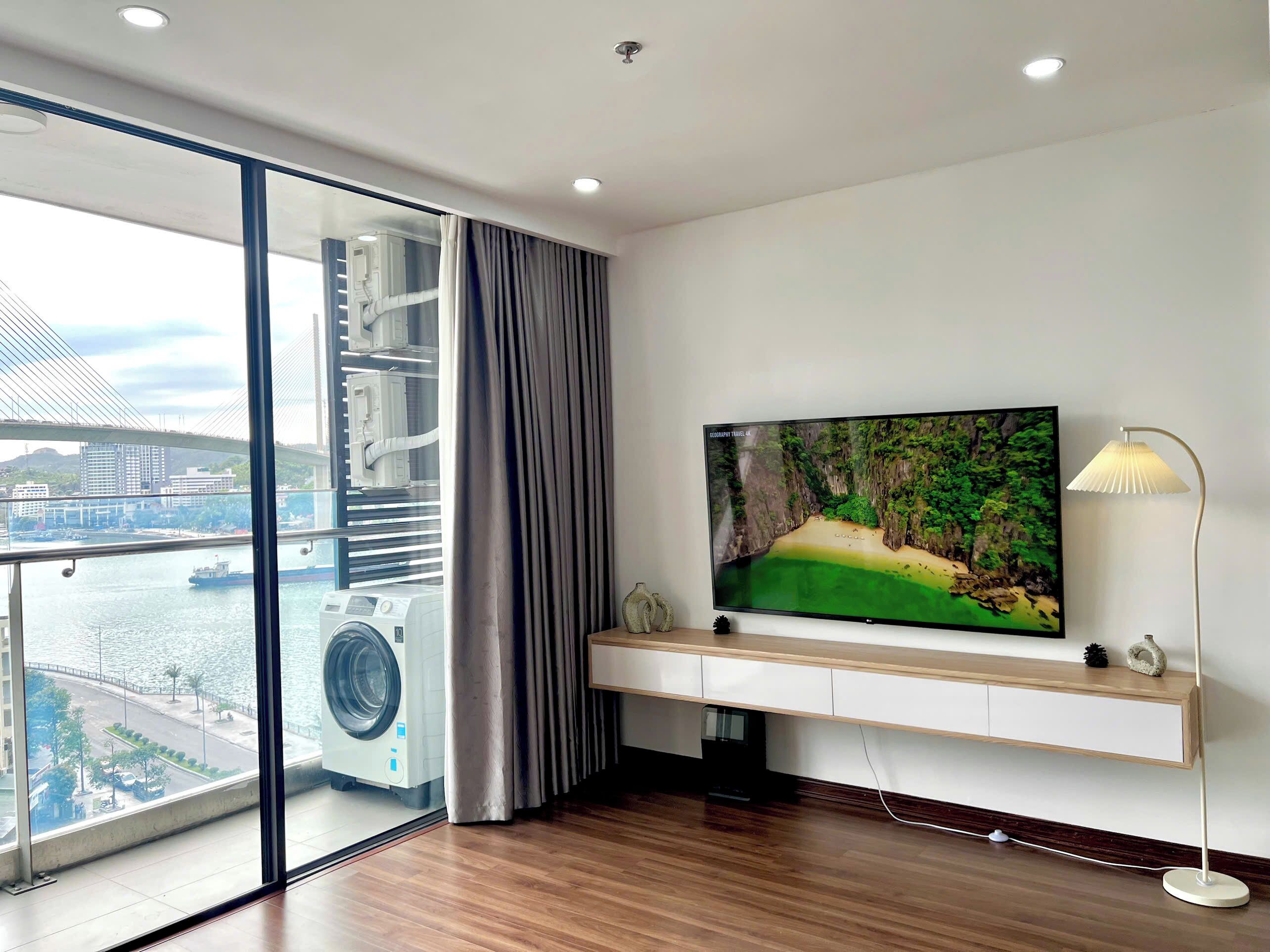 Een moderne hotelkamer met een groot raam, een flatscreen televisie, een staande lamp en een ingebouwde wasmachine en droger.