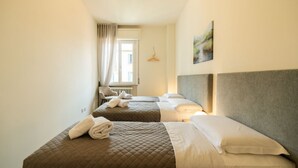 A hotel room with two beds, a radiator, a window with curtains, and a wall-mounted hanger. - Elegant residence overlooking Porta Leoni (Verona)