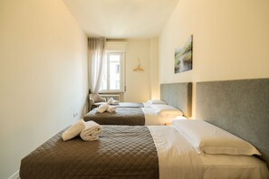Ein Hotelzimmer mit zwei Betten, einem Heizkörper, einem Fenster mit Vorhängen und einem Wandhänger.