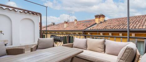 A patio with wicker furniture, a table, and a view of buildings with red-tiled roofs.