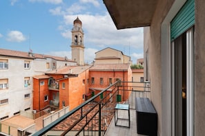 A balcony with a view of a building with a bell tower, a tiled roof, and a clear sky. - Elegant residence overlooking Porta Leoni (Verona)