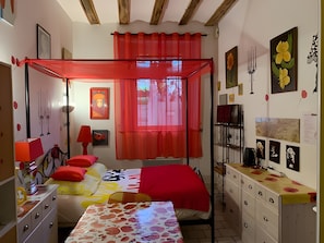 Una habitación con una cama con dosel, un escritorio con cajones, una lámpara y una pared con cuadros enmarcados.