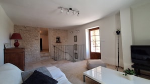 Un saló amb un sofà, una taula de centre, una làmpada, un televisor, una escala i una porta amb finestre.