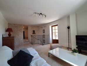 Ein Wohnzimmer mit einer Couch, einem Couchtisch, einer Lampe, einem Fernseher, einer Treppe und einer Tür mit einem Fenster.