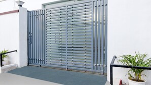 A gated entrance with a metal gate, a potted plant, and a small step leading to a balcony.