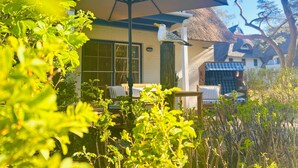 Une terrasse avec une table et des chaises, un bâtiment au toit de chaume et un grand parasol.