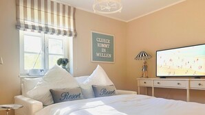 Une chambre à coucher avec un lit, une télévision, une fenêtre avec des rideaux et un tableau accroché au mur.