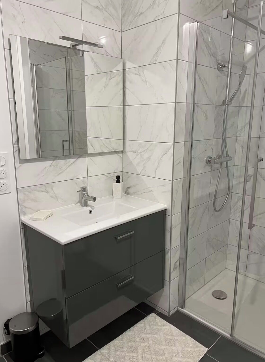 Ein Badezimmer mit einer marmorverkleideten Dusche, einem weißen Waschbecken mit Spiegel darüber und einem dunklen Schrank darunter.
