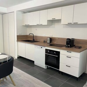 A modern kitchen with white cabinets, a wooden countertop, a black coffee maker, a kettle, and a dishwasher. - Cosy apartment near the station - parking - Near center (Angers)