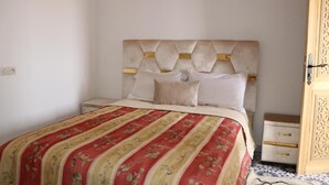 Un letto con copriletto a motivi floreali, una testiera imbottita e un comodino con cassetti.