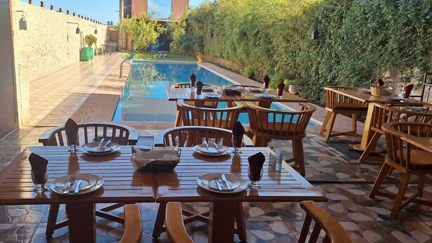 Zona pranzo a bordo piscina con tavoli e sedie, una piscina e un muro in mattoni.