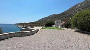Uma área costeira com calçada pavimentada, um muro de pedra e um edifício ao fundo.