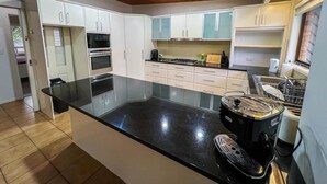 A modern kitchen with a central island, white cabinets, and a wooden ceiling. - Bonhaven Deluxe King Room with private Bathroom (Runcorn)