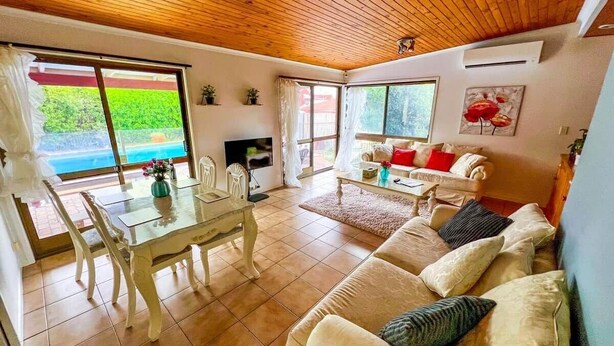A spacious living area with a wooden ceiling, a dining table with chairs, a sofa set, and large windows offering a view of greenery. - Bonhaven Deluxe King Room with private Bathroom (Runcorn)