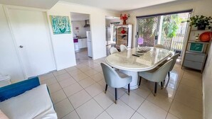 A modern kitchen with white cabinets, a dining area with a glass table, and a view of the outdoors through a sliding door. - Unique Japanese Ensuite Room futon tatami 3 people (Runcorn)