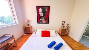 A neatly made bed with white and red bedding, two rolled towels, and a wall art piece. - Unique Japanese Ensuite Room futon tatami 3 people (Runcorn)