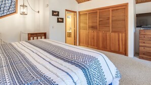 A bedroom with a wooden ceiling, a bed with patterned bedding, a wardrobe, and a television. - Cozy Sunriver Gateway: SHARC, Beautiful Windows, Deck, Games, Bikes (Sunriver)