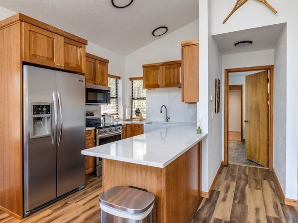 A kitchen with wooden cabinets, stainless steel appliances, a central island, and a trash can.