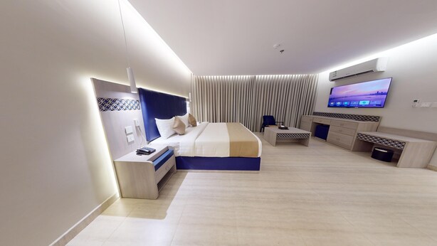 A modern hotel room with a bed, bedside table, TV, and a desk area. - Al Mustarah Hotel (Madinah)