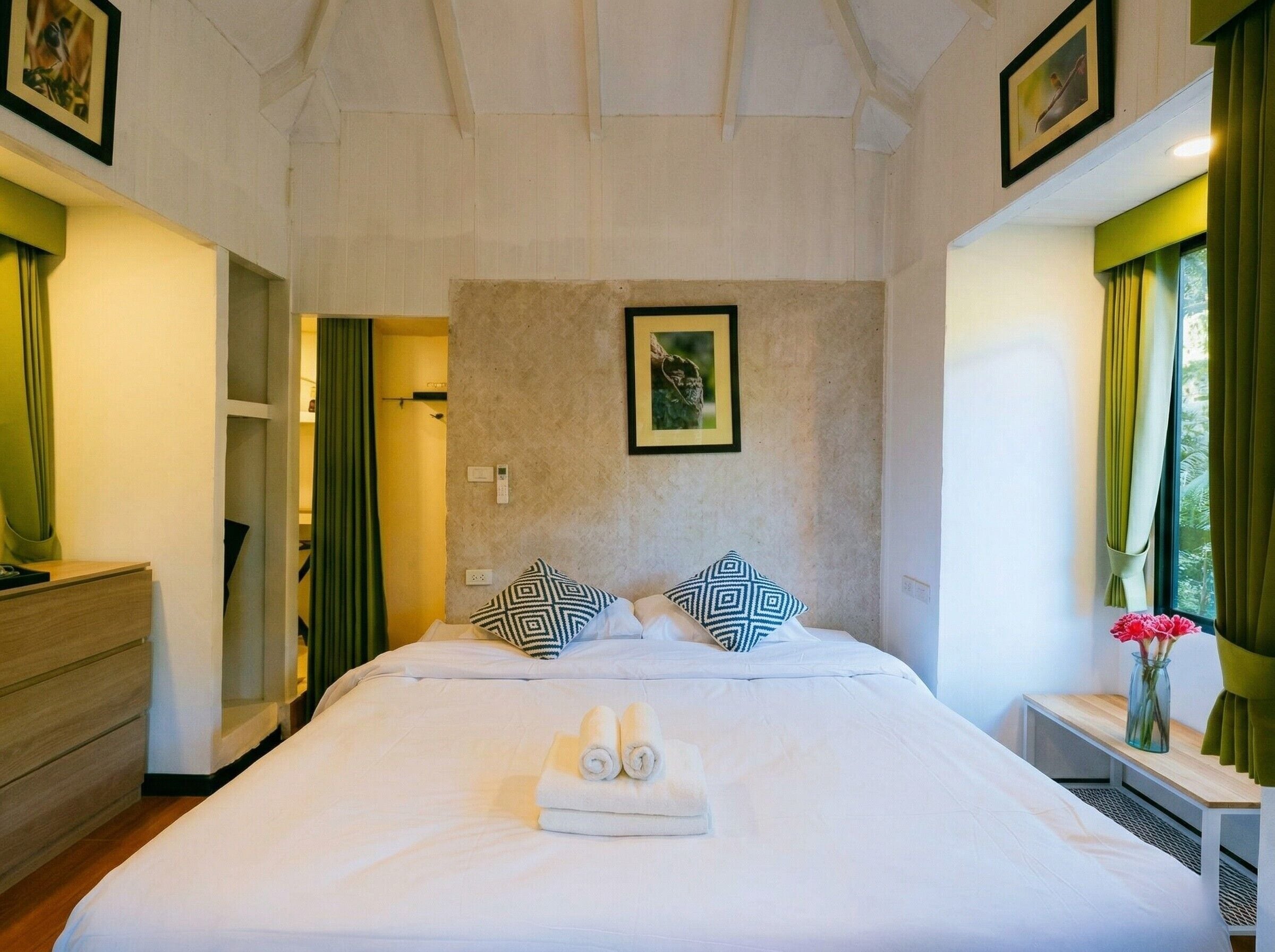 Une chambre d’hôtel avec un grand lit, une table de chevet ornée d’un vase de fleurs et un tableau accroché au mur.
