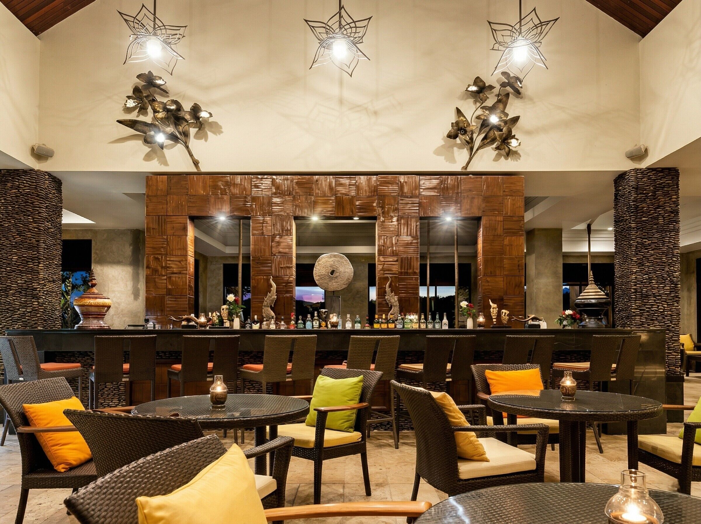 An outdoor bar area with wicker furniture, a stone pillar, and decorative lighting.