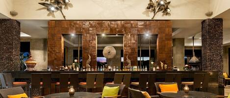 An outdoor bar area with wicker furniture, a stone pillar, and decorative lighting.