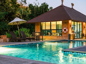 A poolside area with lounge chairs, a table, and a small building with large windows.