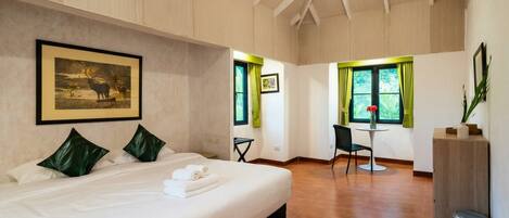 A hotel room with a large bed, a desk, and a chair. There is a framed picture on the wall and a window with curtains.