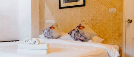 A neatly made bed with white linens, two floral pillows, and a framed picture on the wall.