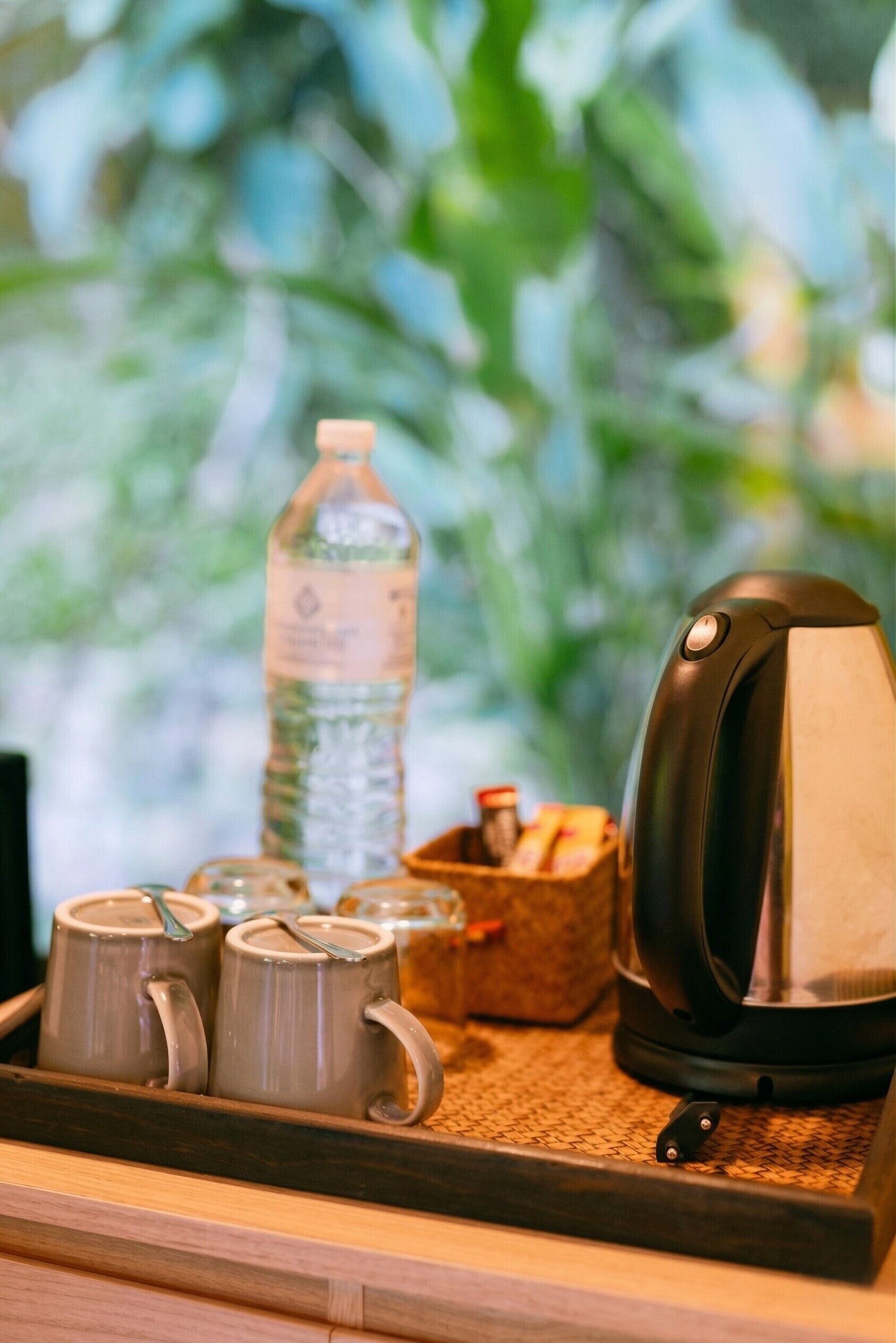 A tray with two mugs, a water bottle, and a coffee maker on a wooden surface.