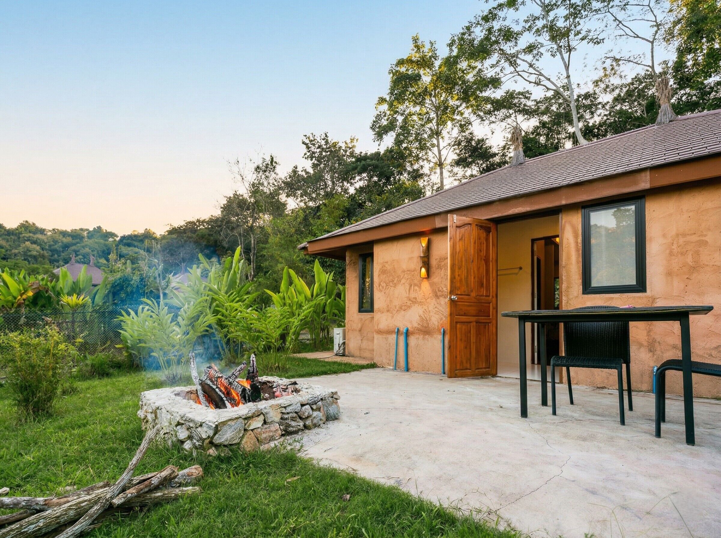 A house with a stone fire pit, a table, and chairs outside.